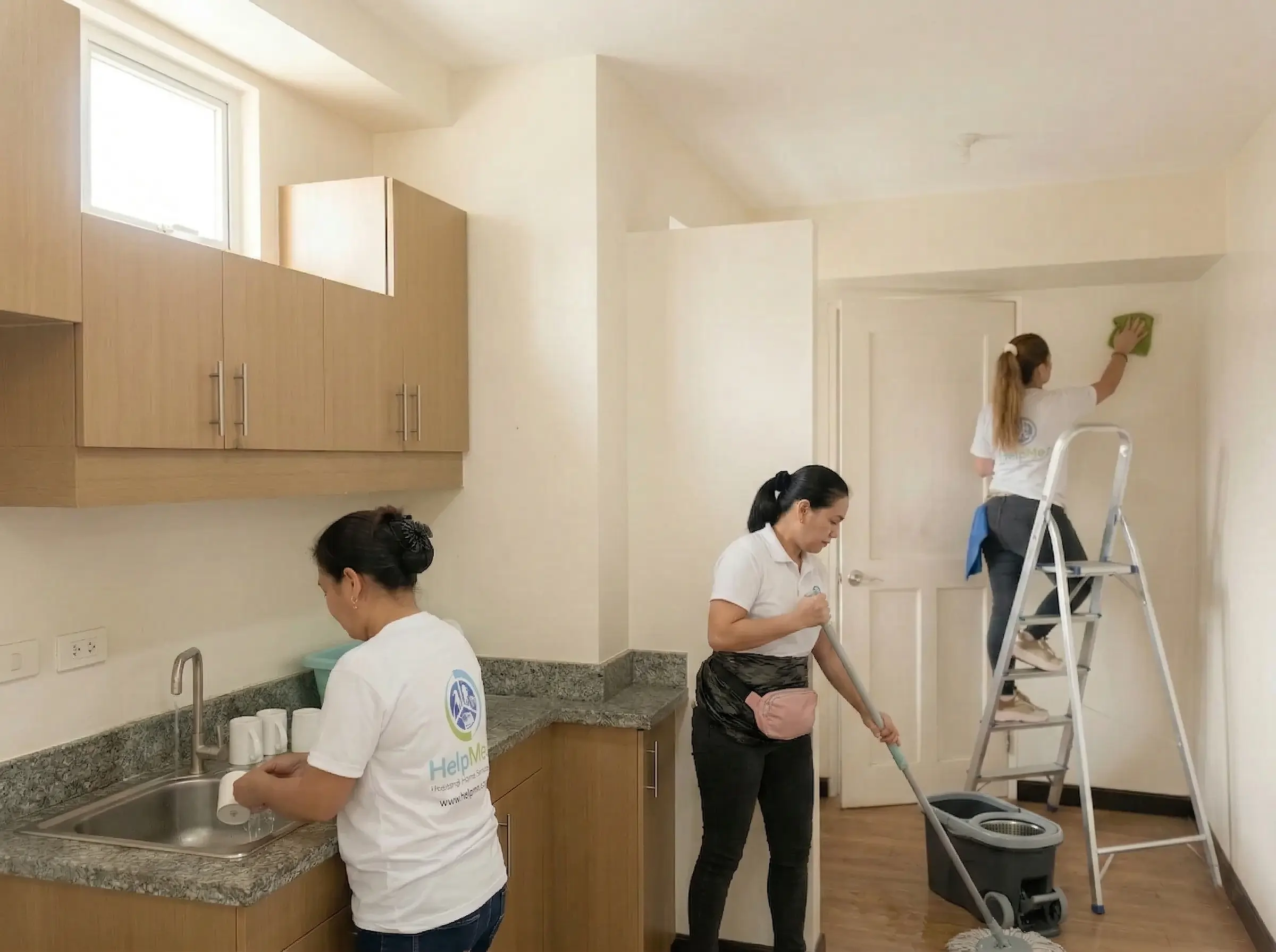 A HelpMeet cleaning team working together in a modern Filipino home — two cleaners at the kitchen sink while teammates on ladders detail high walls and ceiling corners